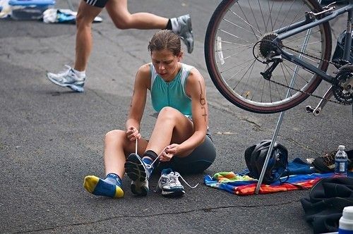 Triathlet tar på löparskor intill sin cykel efter cyklingen